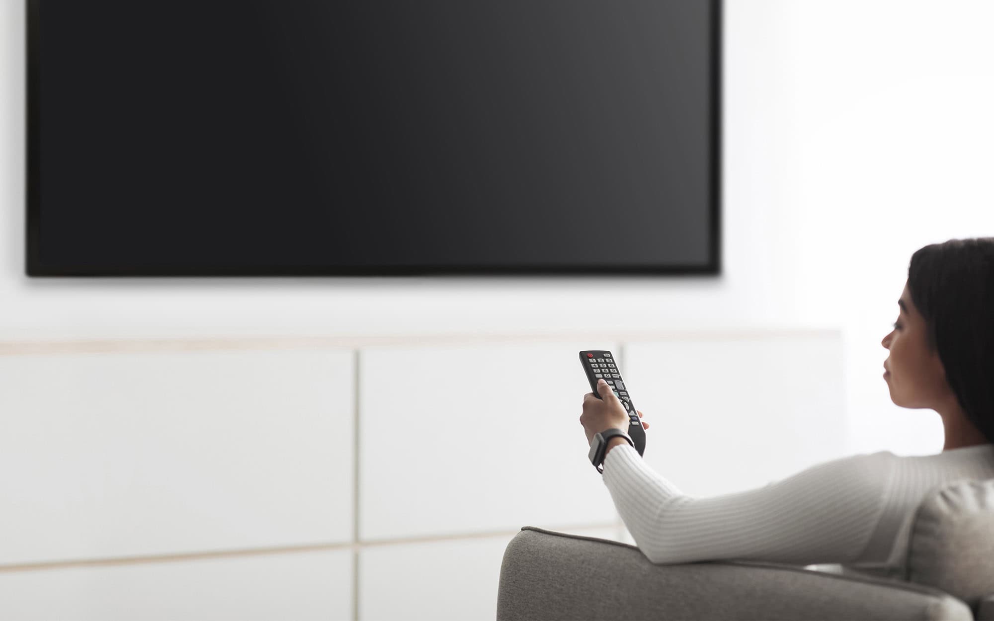 Side view of woman pointing remote at blank tv screen